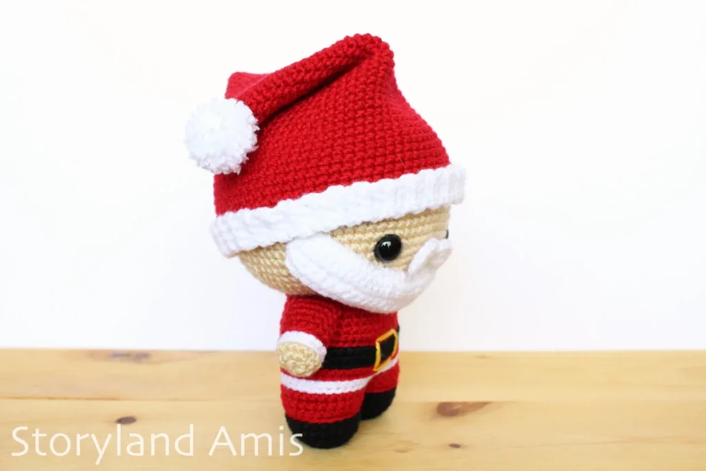 A crocheted amigurumi Santa Claus stands on a wooden table.