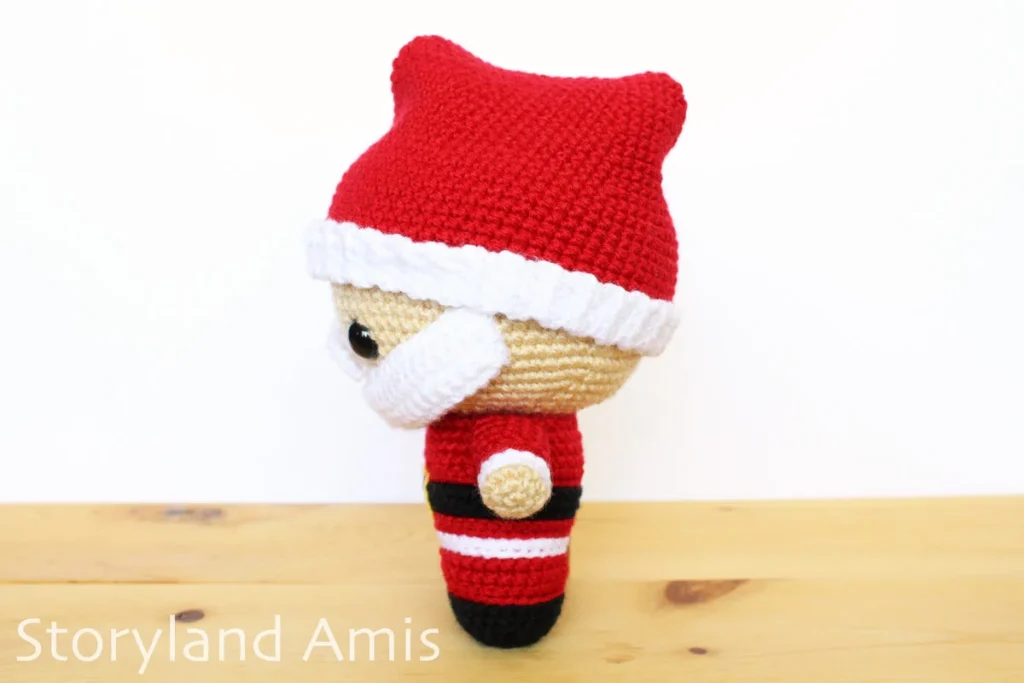 A crocheted amigurumi Santa Claus stands on a wooden table.