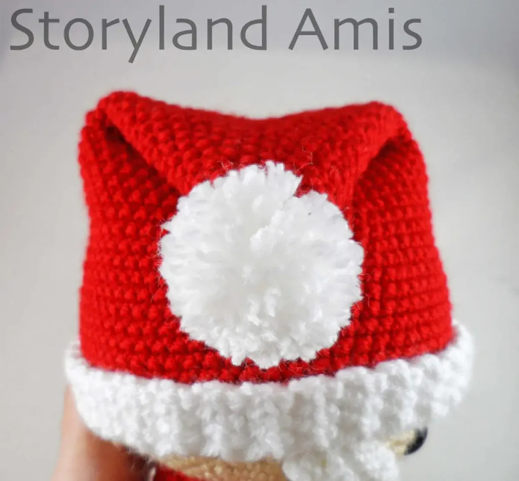 A close-up of a crocheted Santa Claus hat with a pom pom.