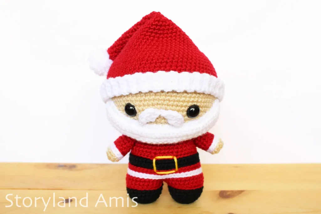 A crocheted amigurumi Santa Claus stands on a wooden table.