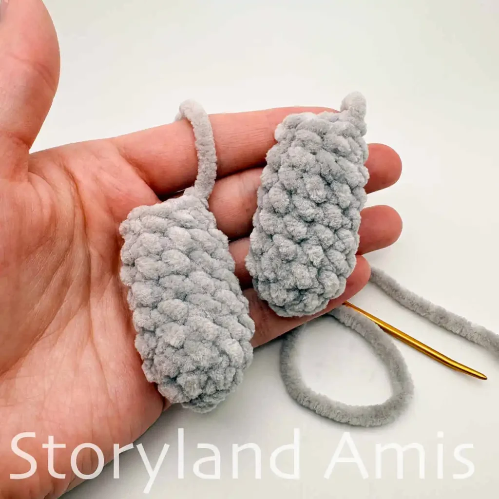 A hand holds two gray crocheted manatee flippers.