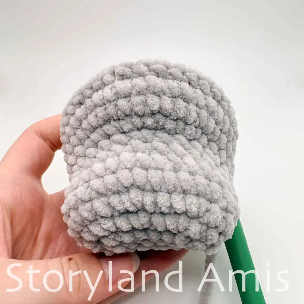 A hand holds a partially finished amigurumi manatee.