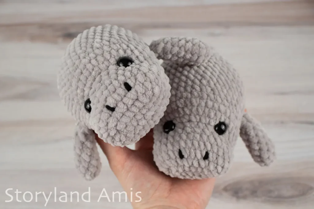 A hand holds two crocheted amigurumi manatee toys.
