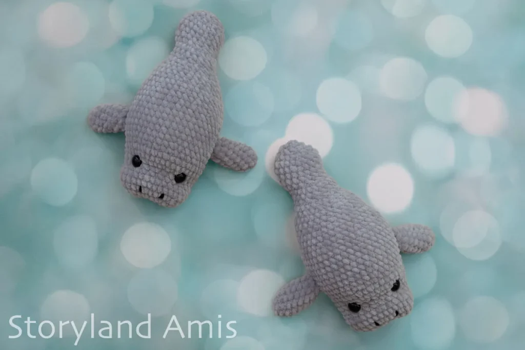 Two crocheted amigurumi manatee toys lie on a blue and white bubble background.