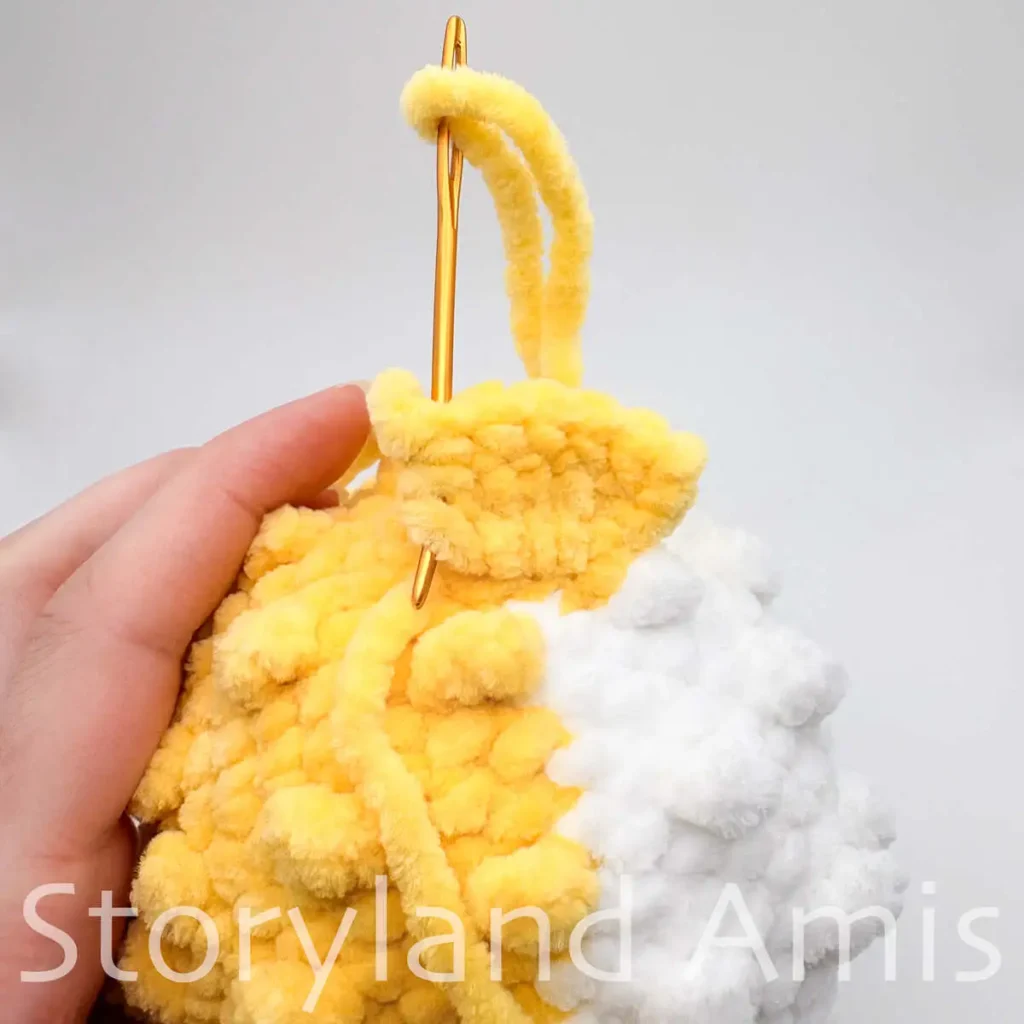 A close-up of a tapestry needle being used to sew a tail fin to the body of an amigurumi pufferfish toy.