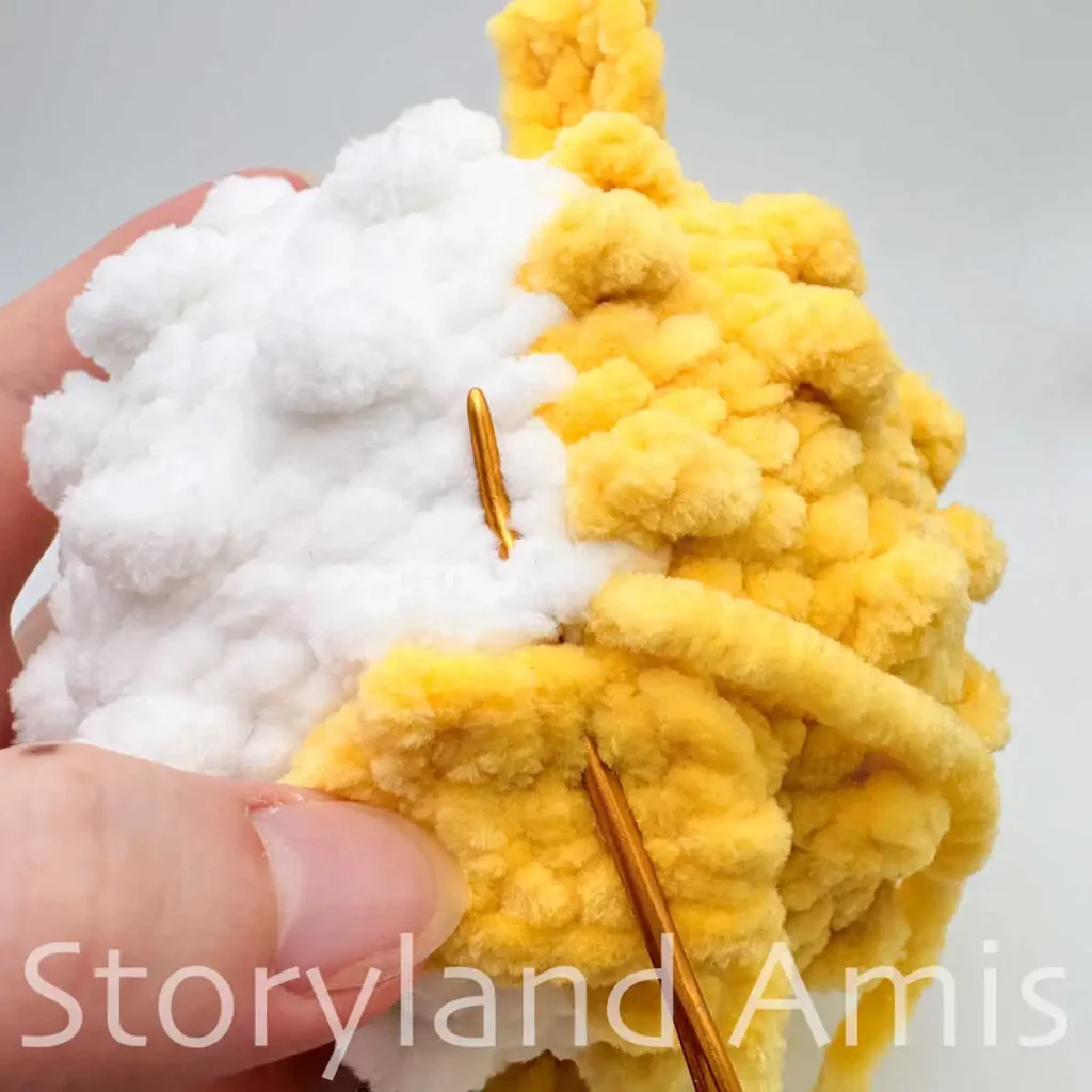 A close-up of a tapestry needle being used to sew a tail fin to the back of an amigurumi pufferfish body.