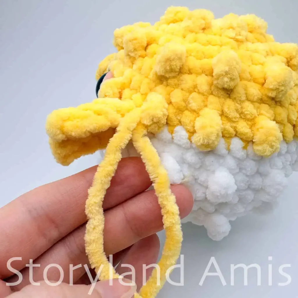 A close-up of the side fin on an amigurumi pufferfish toy. Two yellow yarn tails are hanging from the fin.