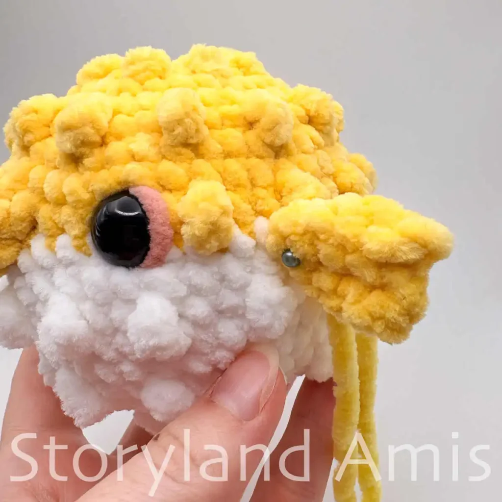 A close-up of a yellow crocheted fin pinned to the body of an amigurumi pufferfish toy.