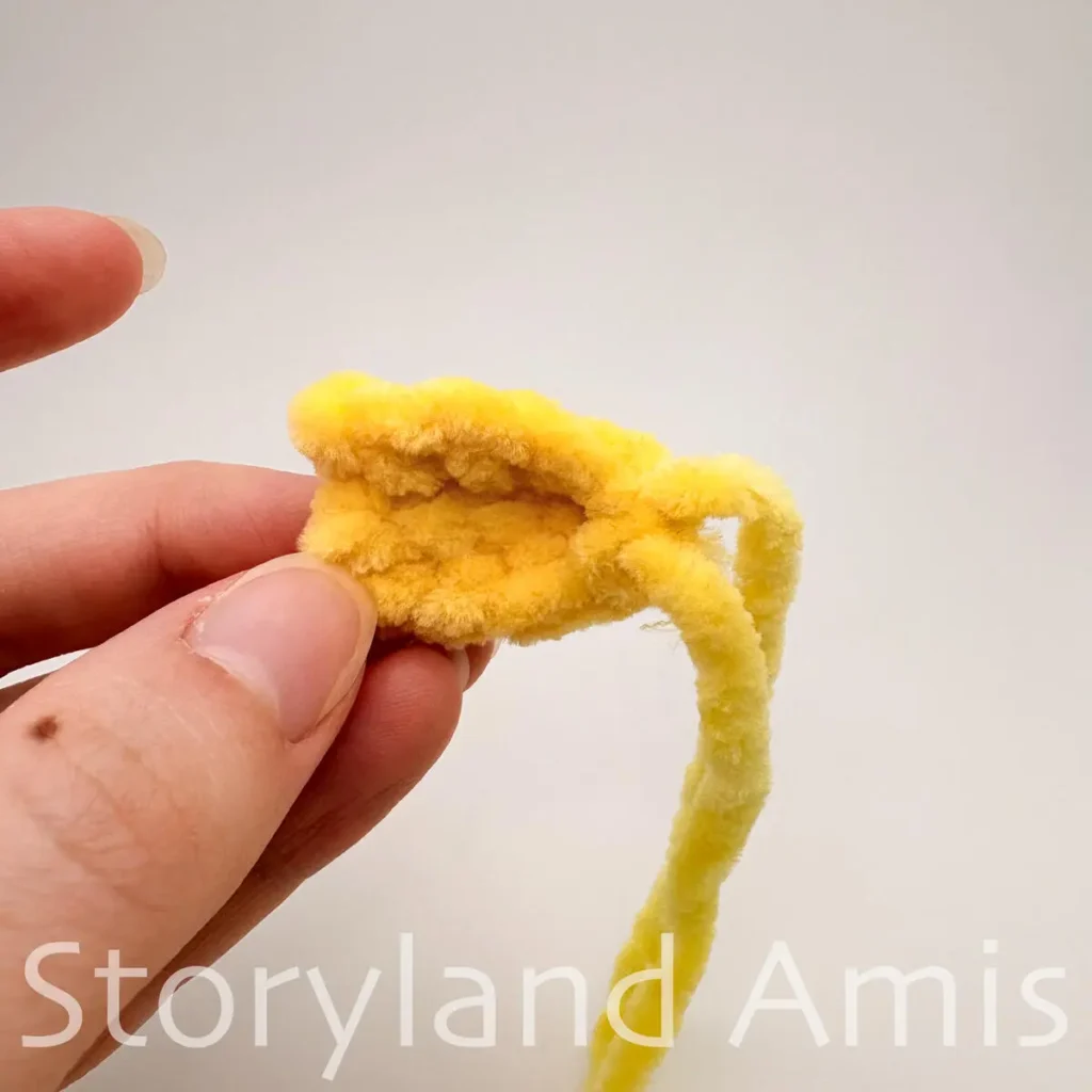 A hand holds a small yellow crocheted fin for an amigurumi pufferfish toy.