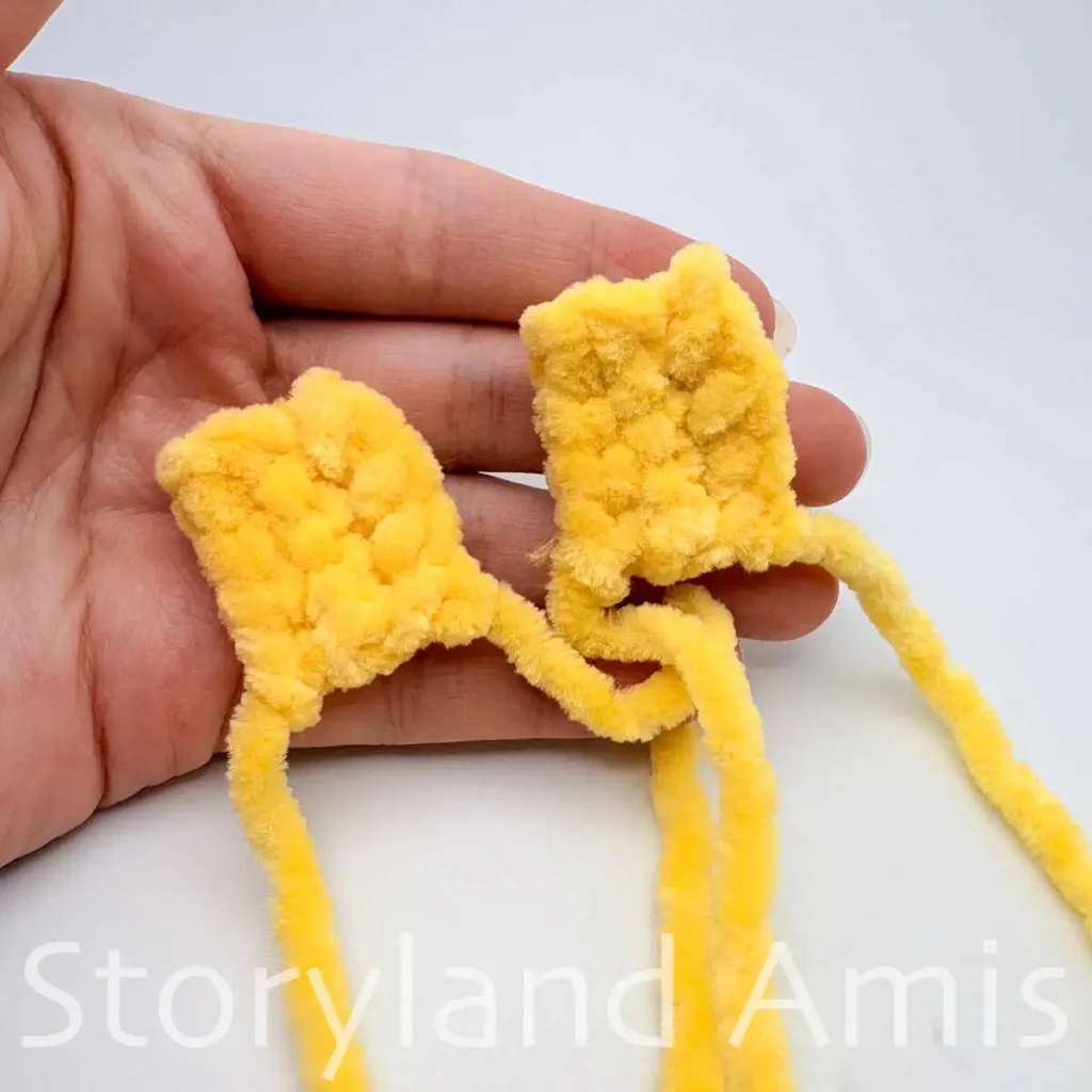 A hand holds two small yellow rectangular crocheted pieces.