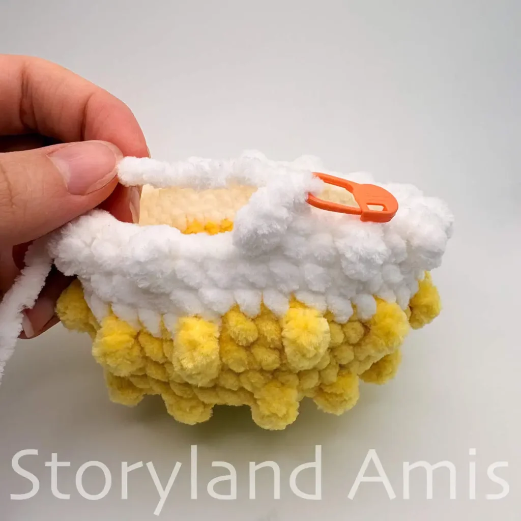 A partially finished crocheted pufferfish toy with an orange stitch marker placed in a stitch.