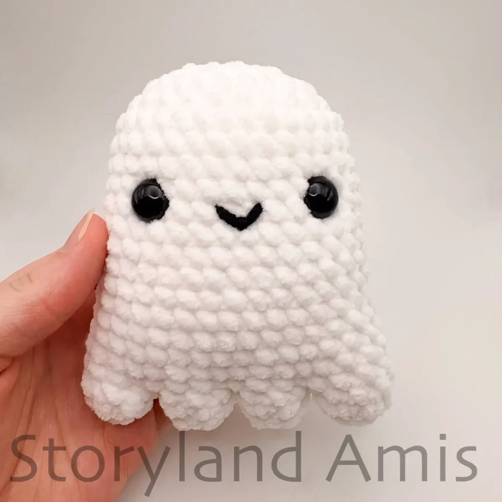 A hand holds a partially finished amigurumi ghost toy.