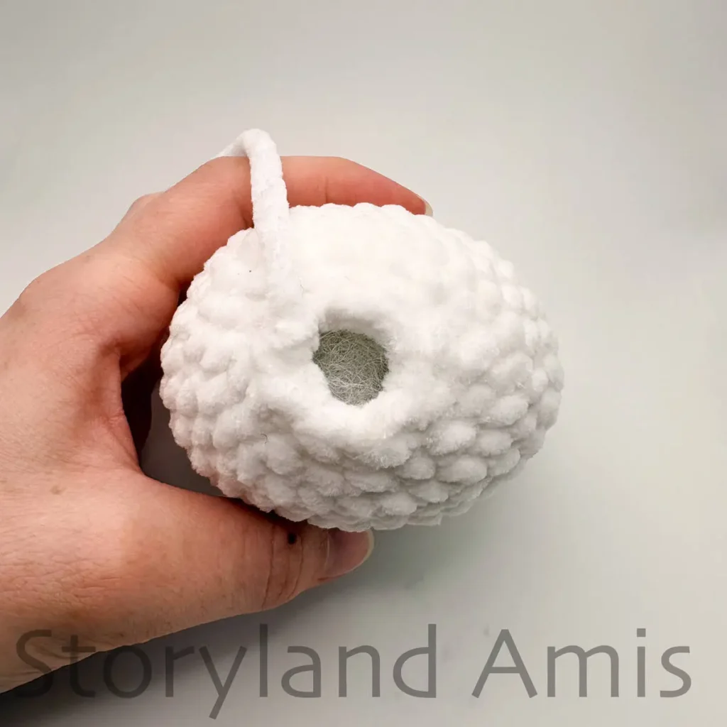 A close-up of the last round on the top of a crocheted amigurumi ghost. The ghost is held steady by a hand.