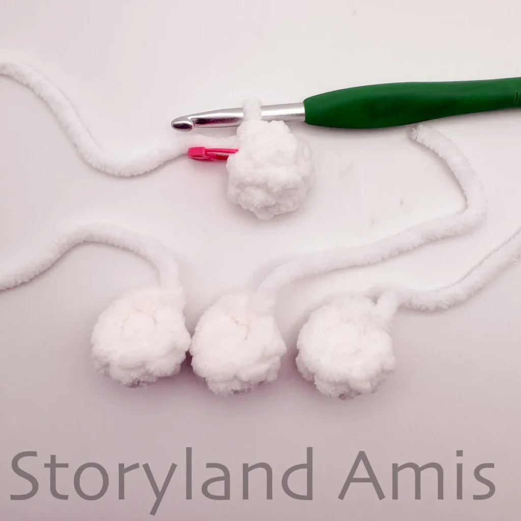 A green crochet hook is attached to a small, round white crocheted piece. Three more small white crocheted pieces are arranged in a row beneath the crochet hook.