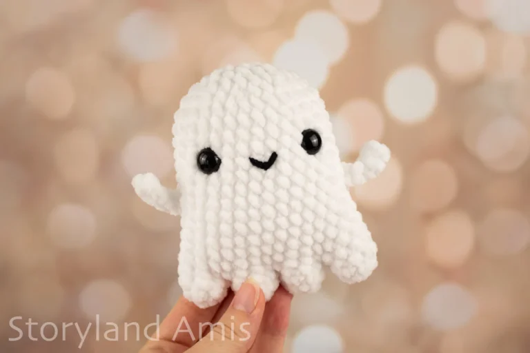 A hand holds up a white crocheted amigurumi ghost toy.