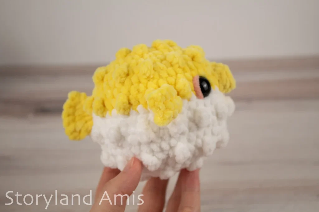 A hand holds an amigurumi pufferfish toy against a wooden background.