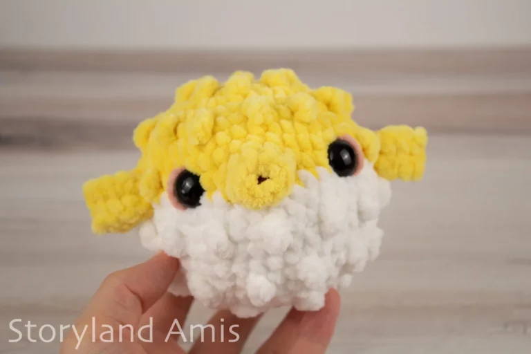A hand holds an amigurumi pufferfish toy against a wooden background.