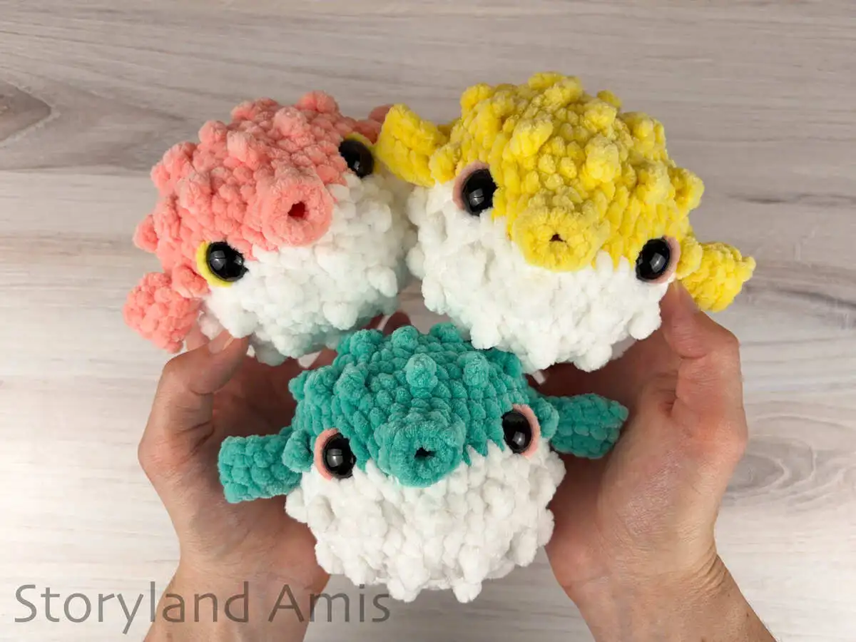 Two hands hold three colorful amigurumi pufferfish against a wooden background.